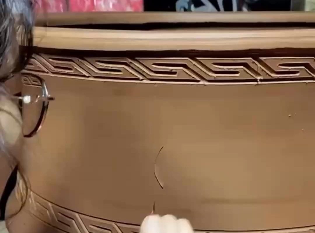 Carving out a flower pattern on a wet clay pot
