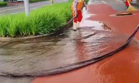 A cleaning worker is directing the water into the sewer with a long piece of cloth
