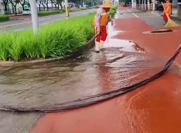 A cleaning worker is directing the water into the sewer with a long piece of cloth
