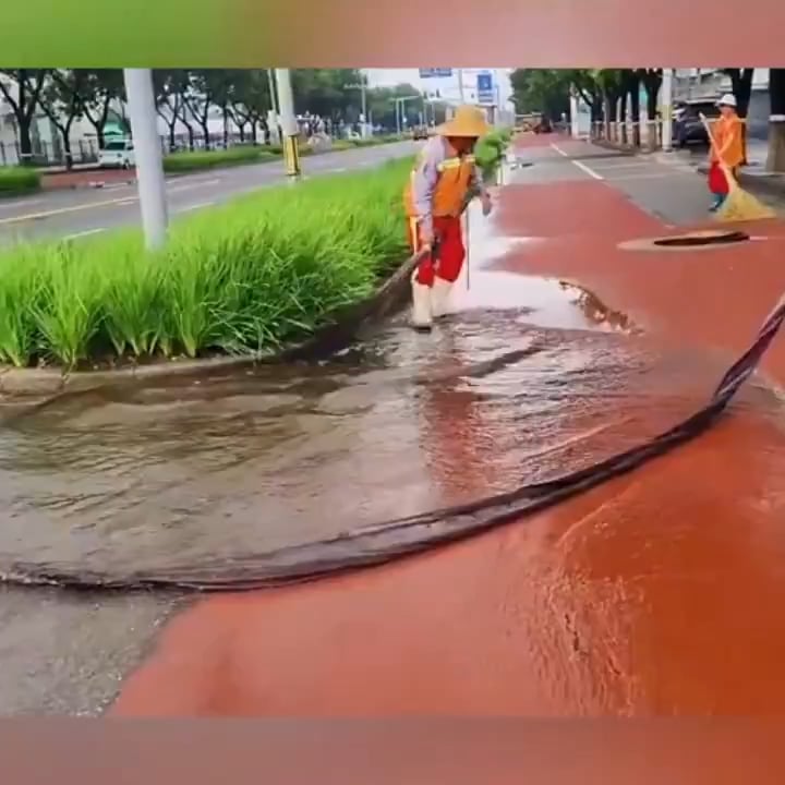 A cleaning worker is directing the water into the sewer with a long piece of cloth