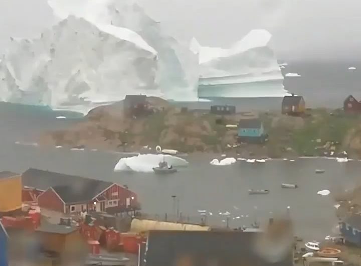 Iceberg casually drifting past a village in Greenland.