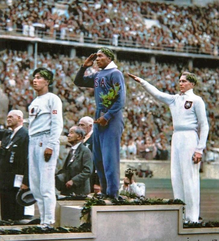Jesse Owens salutes during the presentation of his gold medal for the long jump, after defeating Germany’s Lutz Long during the 1936 Summer Olympics in Berlin (1936) [Colourised]