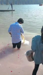 Man performs milk-offering ritual in the Ganges river in India while poor hungry children try to collect it to drink.