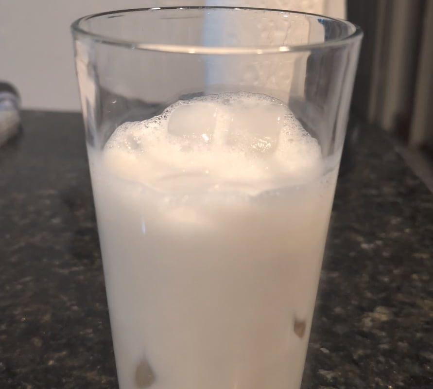 Pouring a shaken espresso shot over iced oat milk