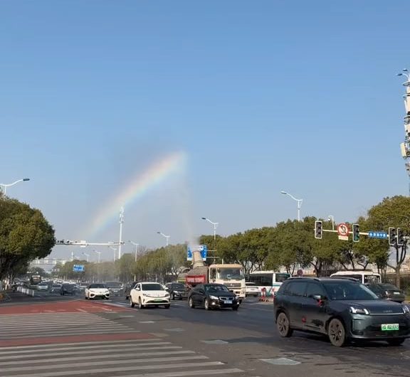 The sprinkler truck leaves a rainbow in its wake.
