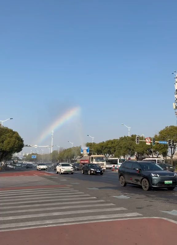 The sprinkler truck leaves a rainbow in its wake.