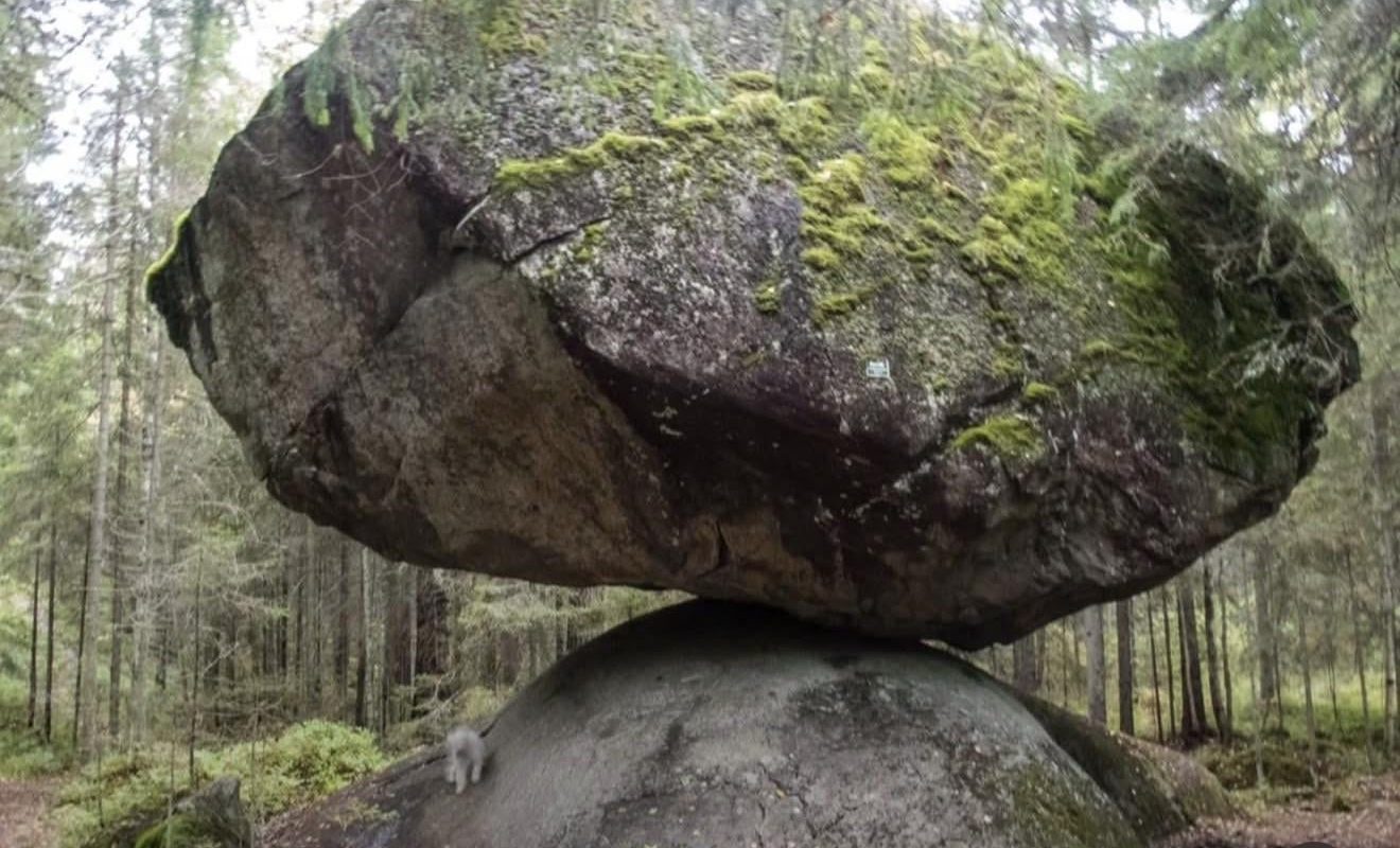 This giant boulder naturally balancing itself on top of a smaller rock in a Finnish forest