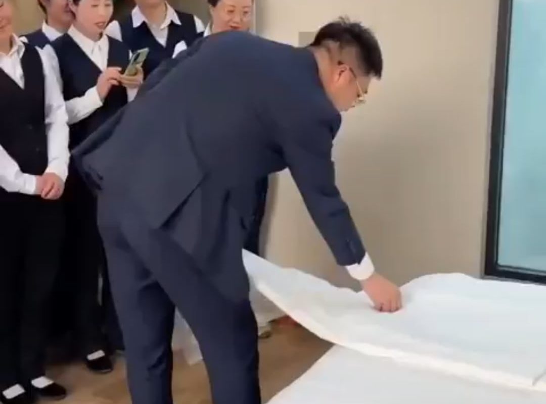 This man shows new hotel staff how to make a bed