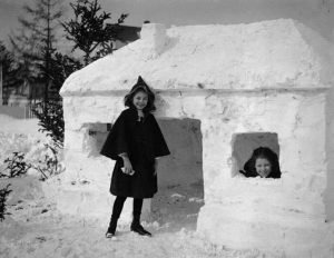 Two girls smile in their snow fort, circa 1910.