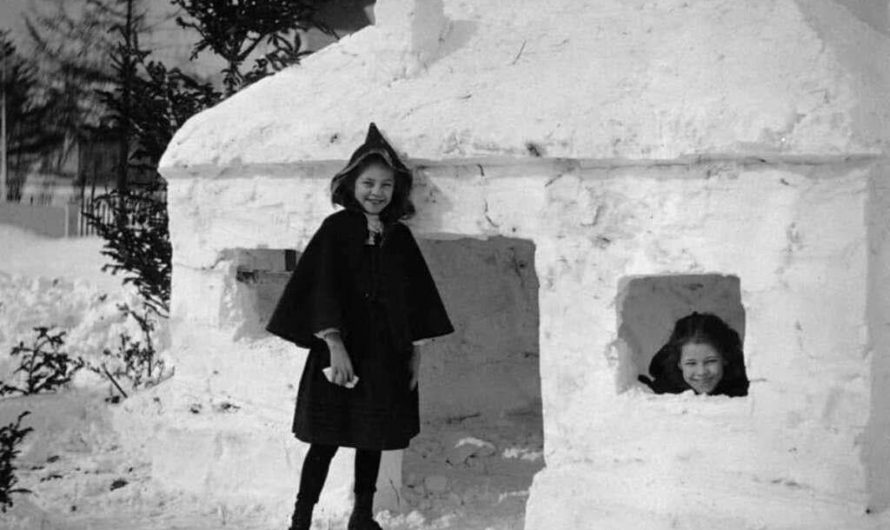 Two girls smile in their snow fort, circa 1910.