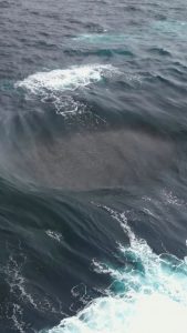 A powerful wave uprising due to small waves colliding to a big rock under water