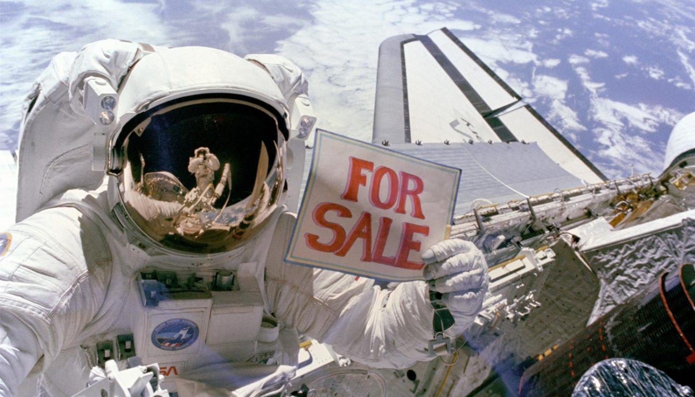 Astronaut Dale A. Gardner holds up a "For Sale" sign as a joke, pretending to offer up two failed satellites, Palapa B-2 and Westar 6, which were retrieved in space during the shuttle Discovery's STS-51A mission in 1984. Astronaut Joseph P. Allen IV can be seen reflected in Gardner's helmet visor.
