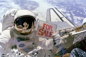Astronaut Dale A. Gardner holds up a "For Sale" sign as a joke, pretending to offer up two failed satellites, Palapa B-2 and Westar 6, which were retrieved in space during the shuttle Discovery's STS-51A mission in 1984. Astronaut Joseph P. Allen IV can be seen reflected in Gardner's helmet visor.