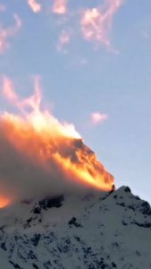 A mountain peak in southwestern China appears to be on fire as sunset light illuminates clouds and blowing snow