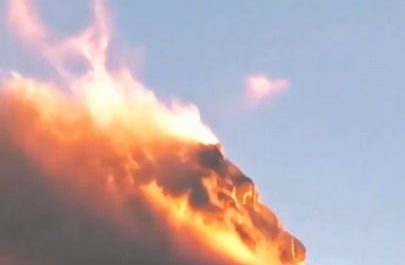 A mountain peak in southwestern China appears to be on fire as sunset light illuminates clouds and blowing snow