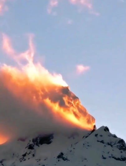 A mountain peak in southwestern China appears to be on fire as sunset light illuminates clouds and blowing snow