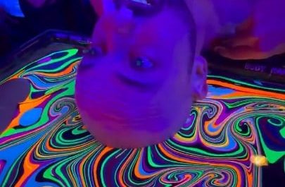Bald man dips his head in liquid rainbow colours