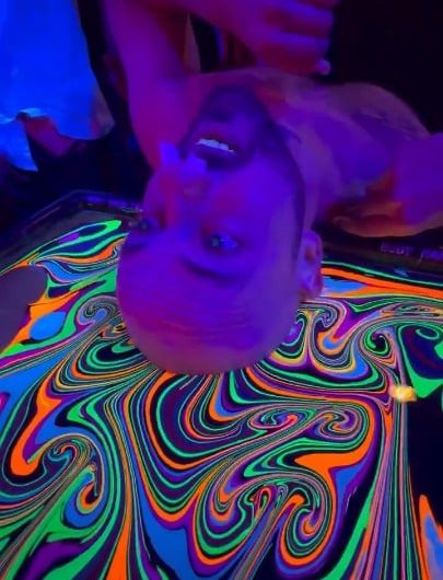 Bald man dips his head in liquid rainbow colours