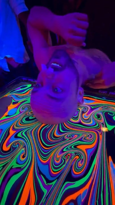 Bald man dips his head in liquid rainbow colours