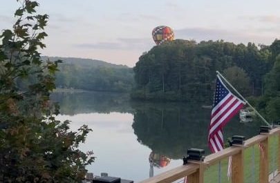 Hot air balloon pilot, dunks the basket in a quiet cottage lake before rising back into sky