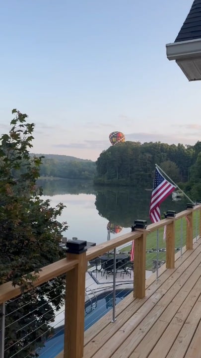 Hot air balloon pilot, dunks the basket in a quiet cottage lake before rising back into sky